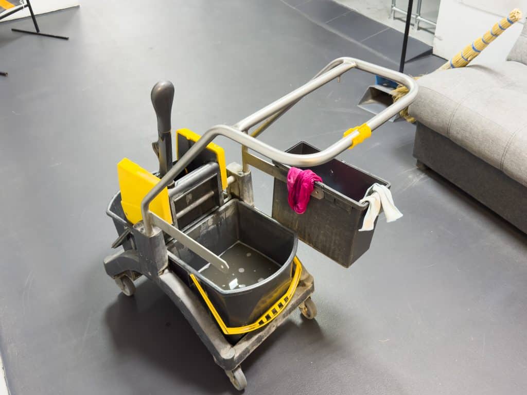 Scopa, mocio o attrezzature per la pulizia domestica, utili per la protezione da germi e batteri o per la sicurezza. Strumenti per le pulizie appoggiati su un pavimento sporco, pronti per iniziare le faccende in appartamento.