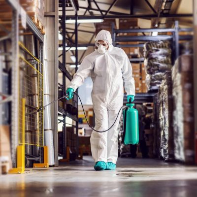 uomo con tuta che sanifica gli ambienti di un capannone industriale